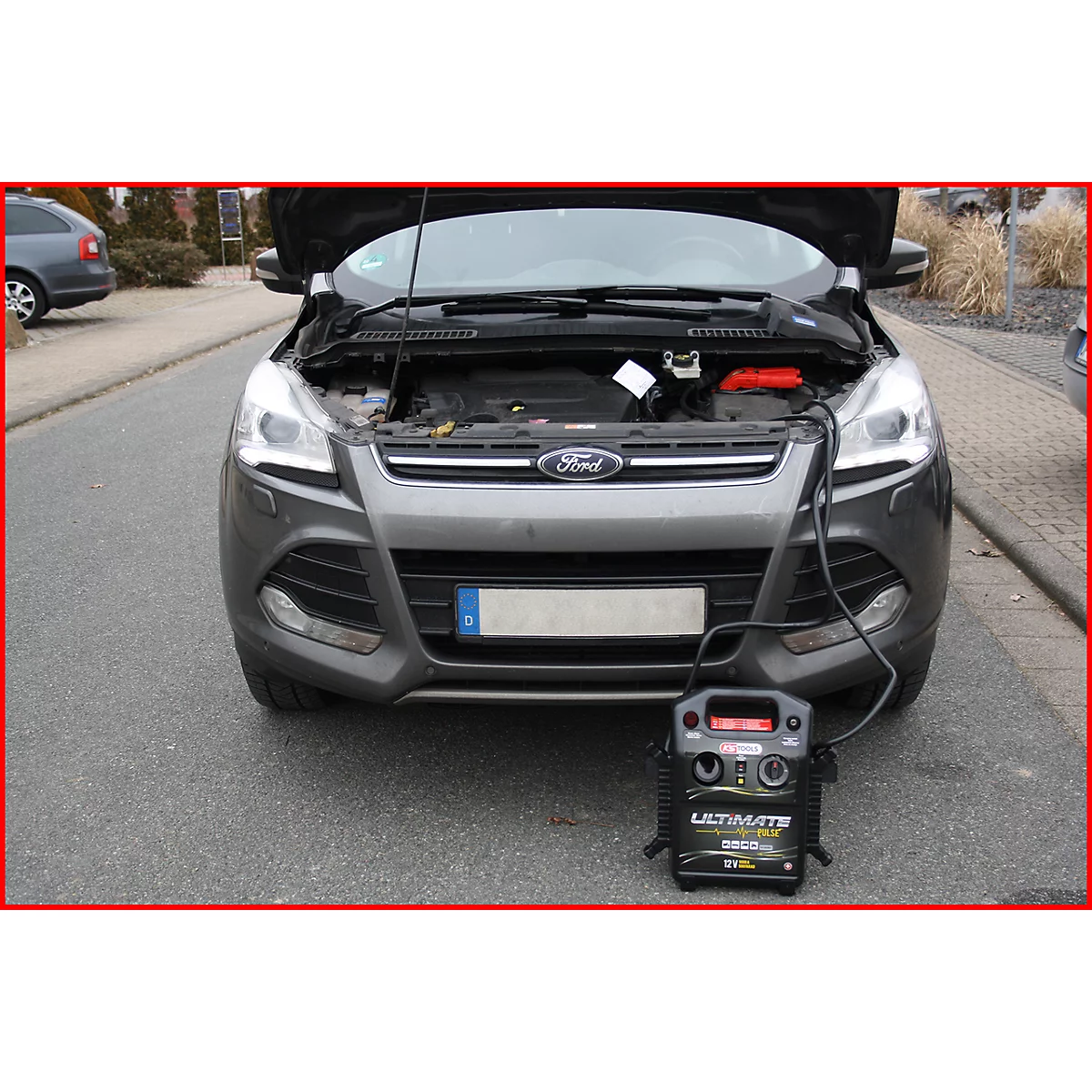 Graues Ford-Auto mit offener Motorhaube, verbunden mit einem Ultimate-Ladegerät auf der Straße.